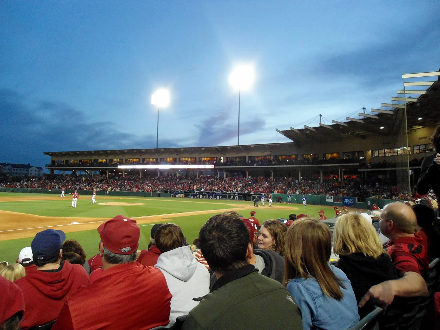 Spectators watching Arkansas and LSU at Baum Stadium under evening floodlights.