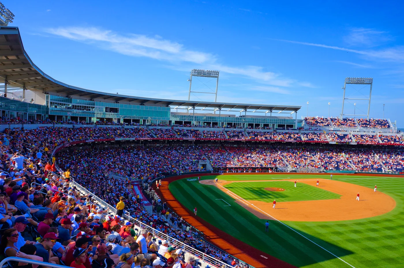 Crowded Omaha baseball grandstands surrounding the diamond on a sunny day.